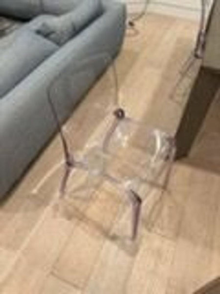 1. Transparent acrylic dining chair placed on a wooden floor next to a gray sofa in a modern living space.