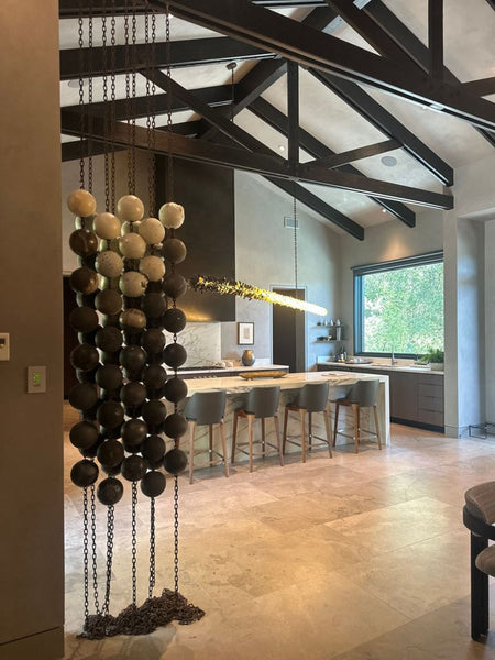 Rows of earthy ceramic spheres linked by oxidized steel chains form a modern Kelly Farley sculpture.