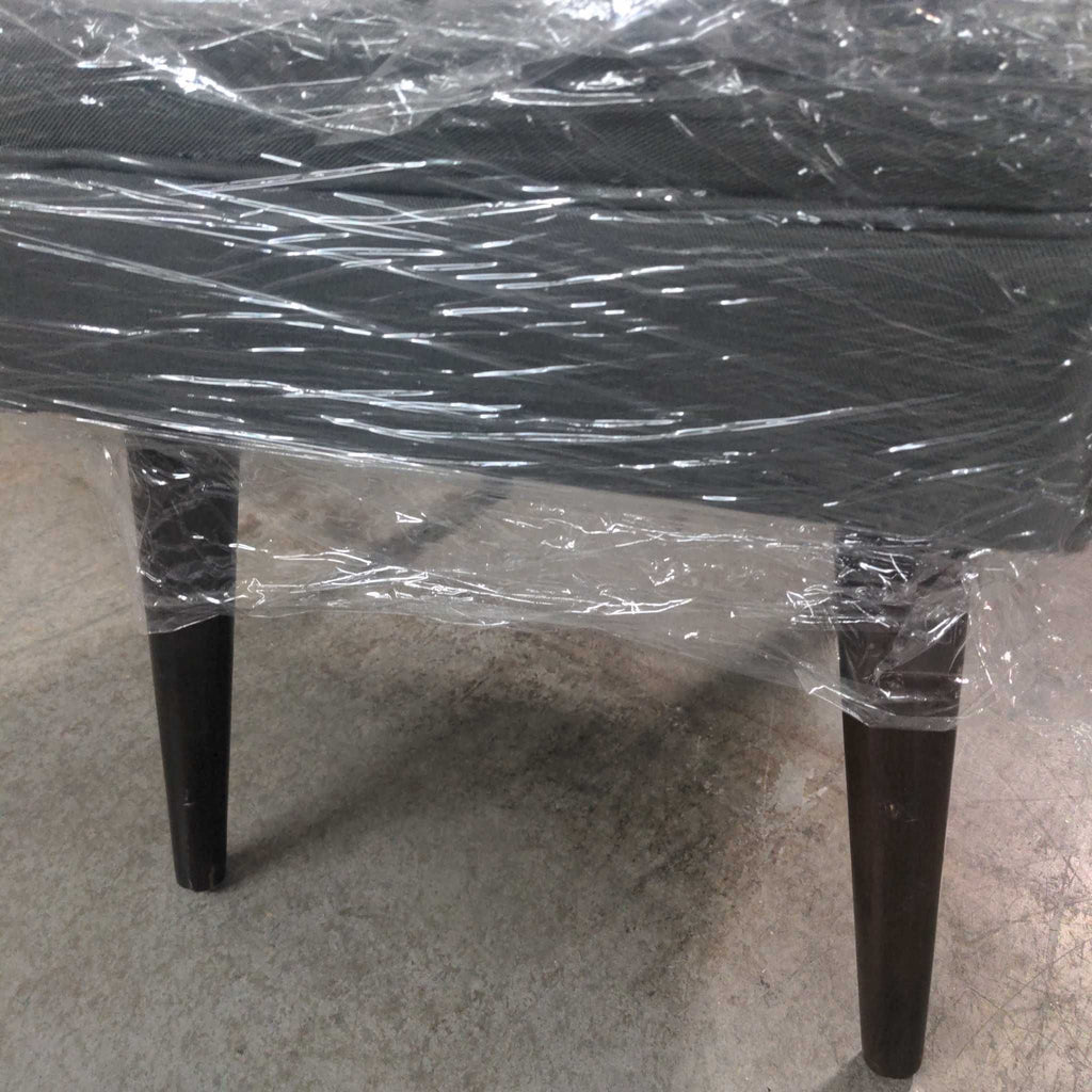 2. Close-up of the legs and lower section of a gray bench, still covered in protective plastic wrap.