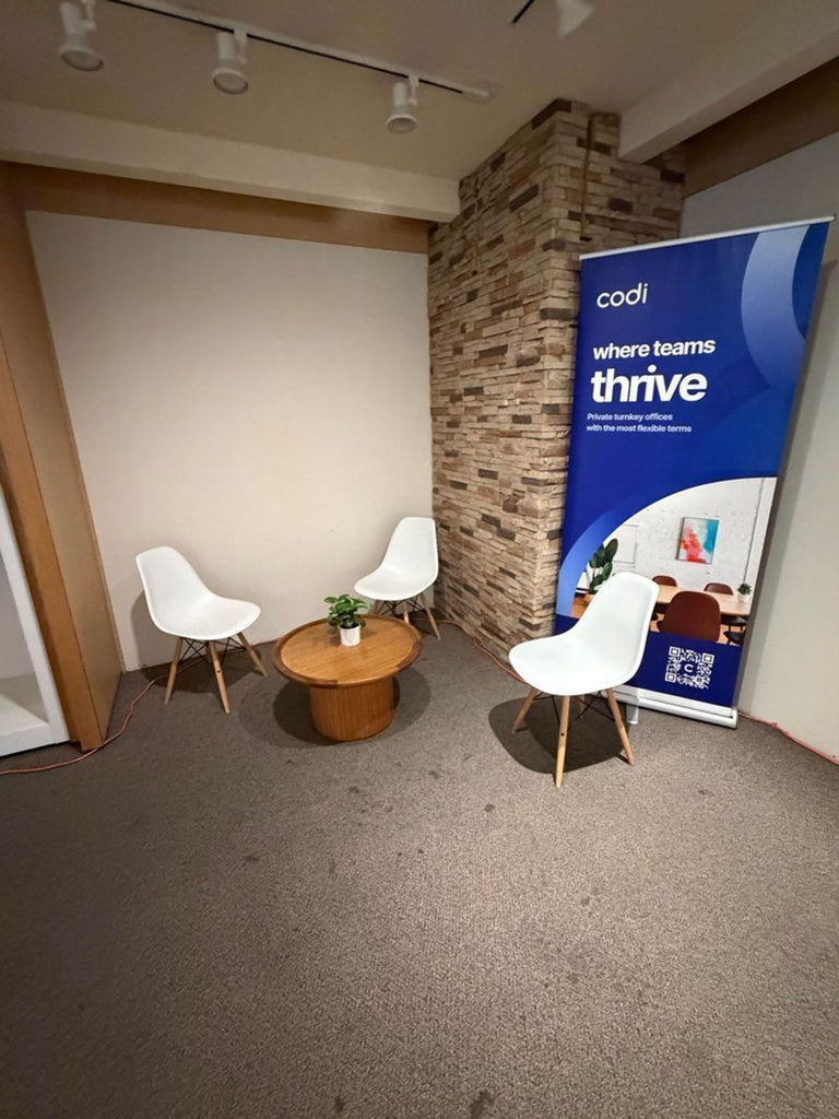 Three modern white dining chairs with wooden legs arranged around a small round table in an office corner.