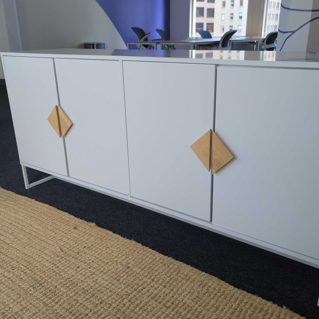 Modern white sideboard with four doors and diamond-shaped wooden handles, standing on metal legs.