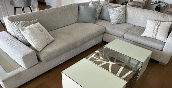 Light gray sectional with matching cushions in a modern living room, featuring a glass-top coffee table in front.