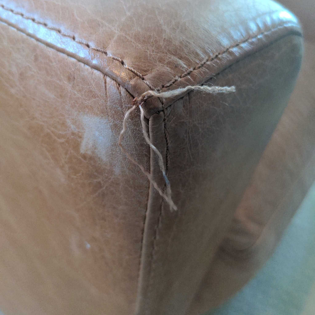 3. Detailed corner of a Westelm tan leather lounge chair, highlighting stitching and a loose thread.