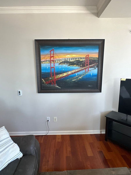 1. Framed painting of the Golden Gate Bridge hanging on a wall above a couch and beside a TV in a living room.