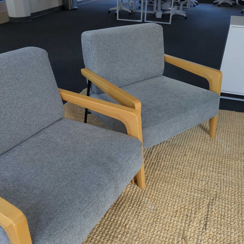 1. Two gray lounge chairs with light wood arms are placed on a textured rug in a modern lounge area.  