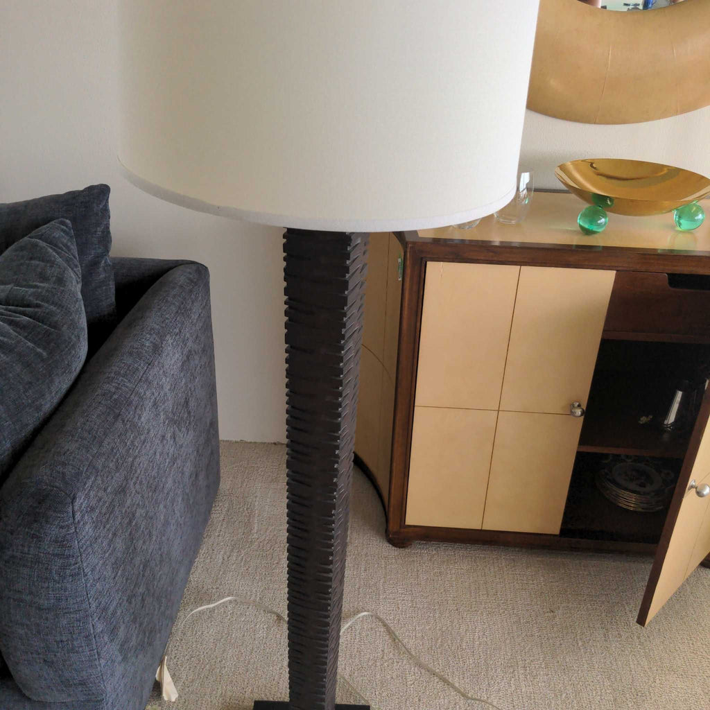 2. Floor lamp with a cylindrical grooved dark stand and a large white lampshade beside a sofa and cabinet.