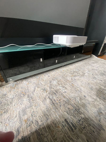 1. Black glass entertainment center with a glass top and electronics placed on top, set on a patterned rug.
