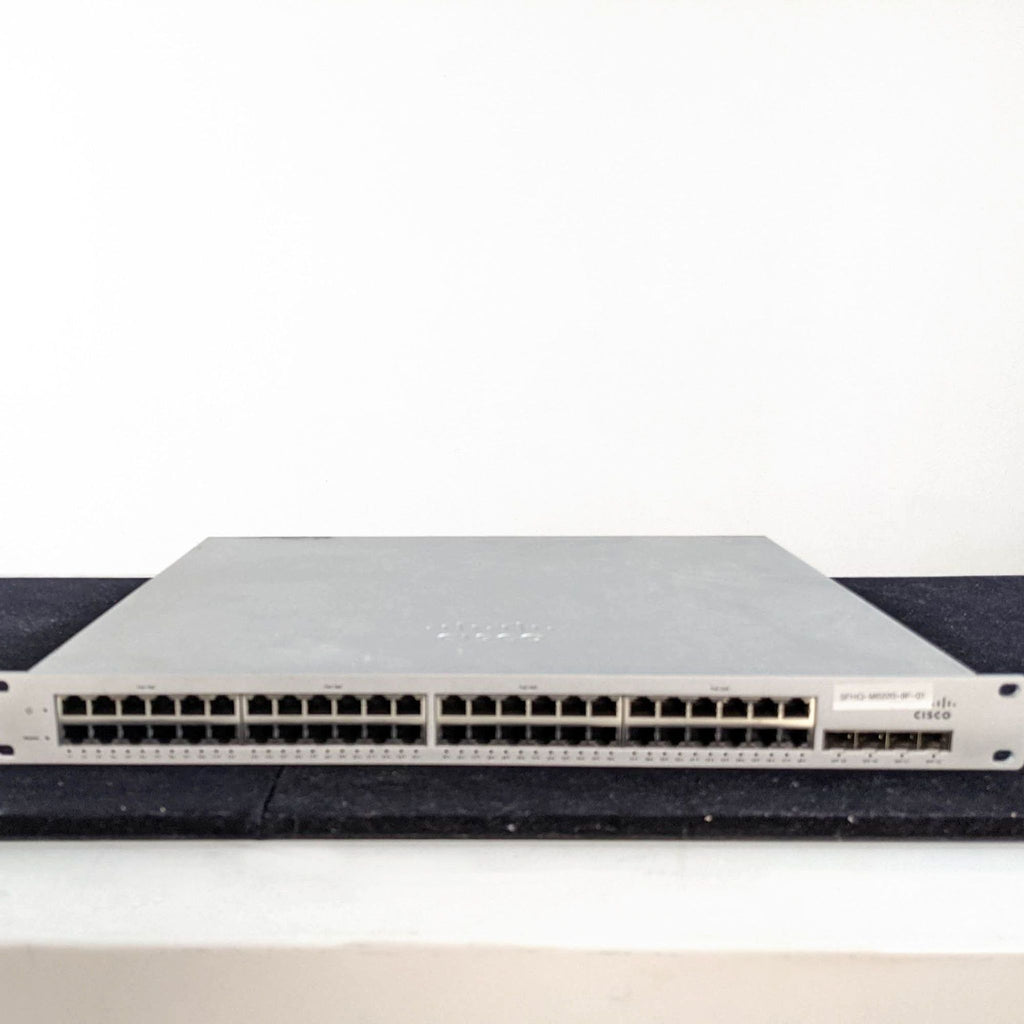 A Cisco & Bros. networking switch with multiple Ethernet ports shown on a black surface against a white wall.  