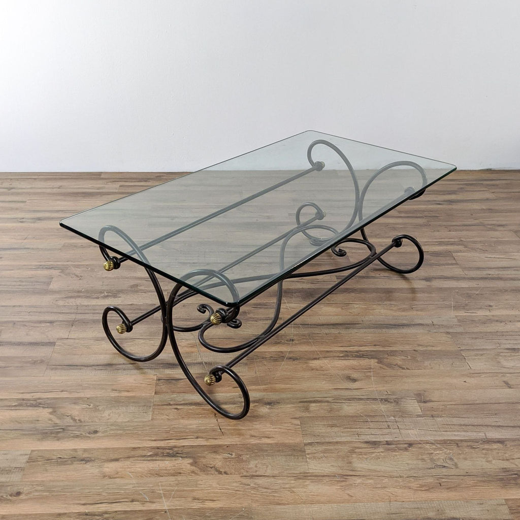 Metal coffee table with a glass top, featuring an ornate scroll base with brass accents.