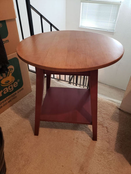 1. Round wooden end table with angled legs and lower shelf, placed on carpet near a window and cardboard boxes.