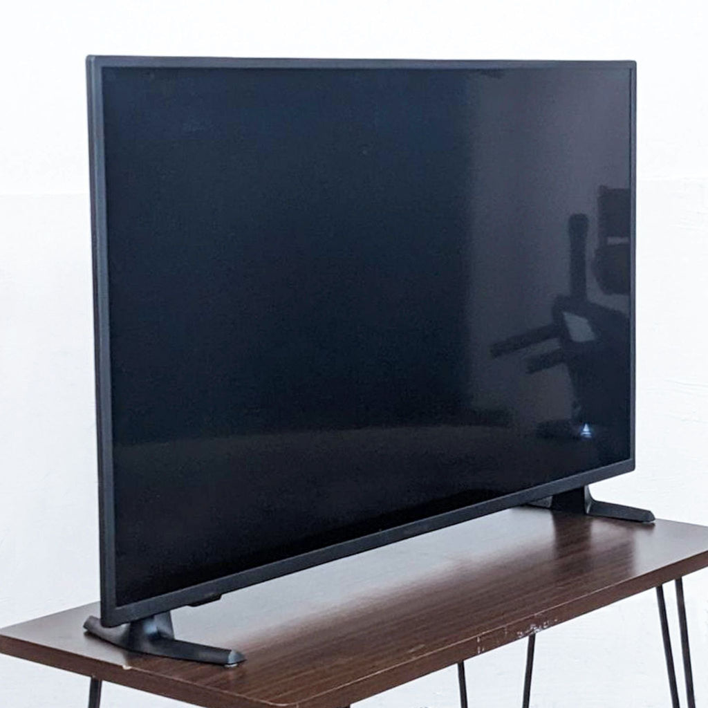 Insignia TV on a wooden stand against a white wall, screen off reflecting a silhouette.