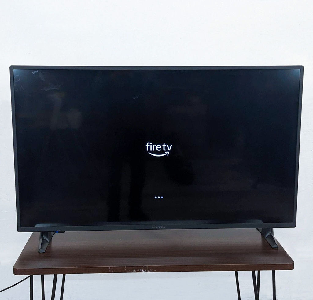 Insignia brand TV on a wooden stand displaying Fire TV logo on the screen.