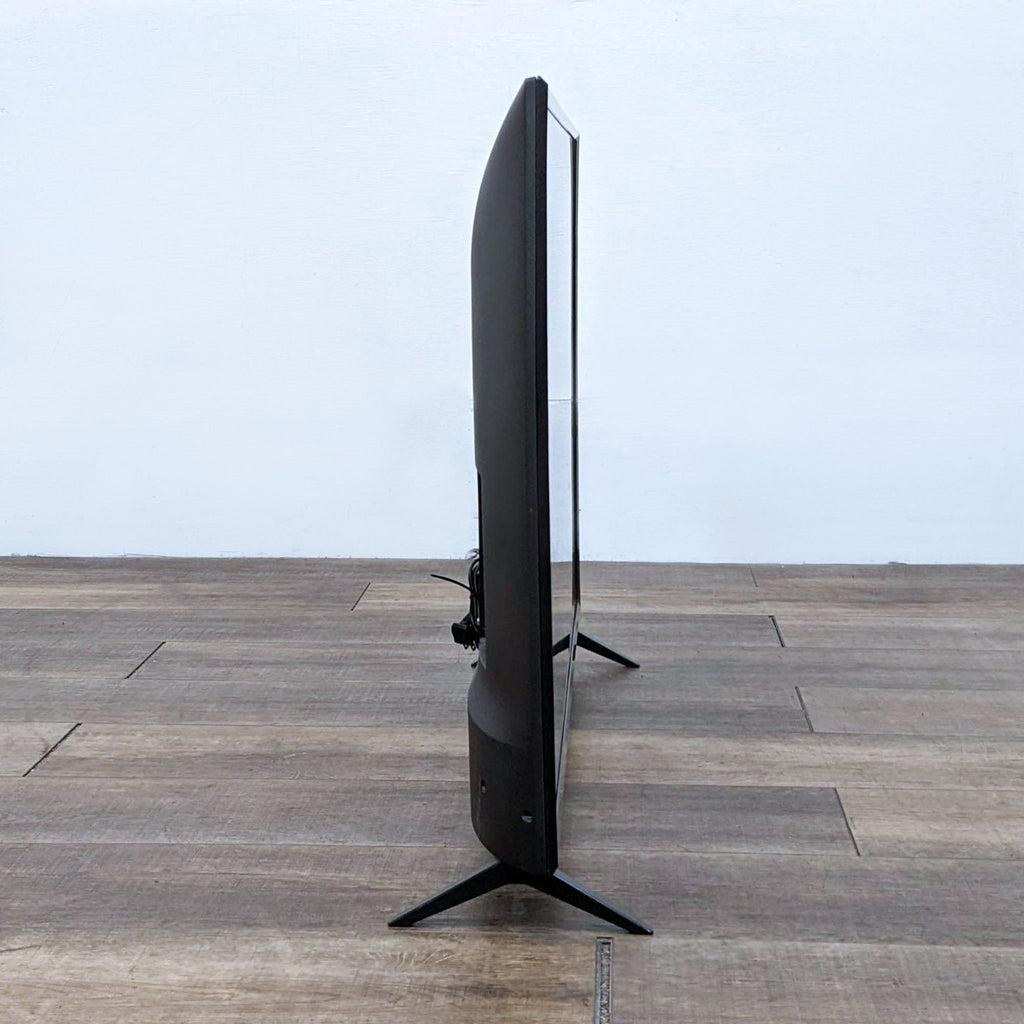 Side view of an LG television on a stand, displaying its thin profile, against a white wall and wood floor.