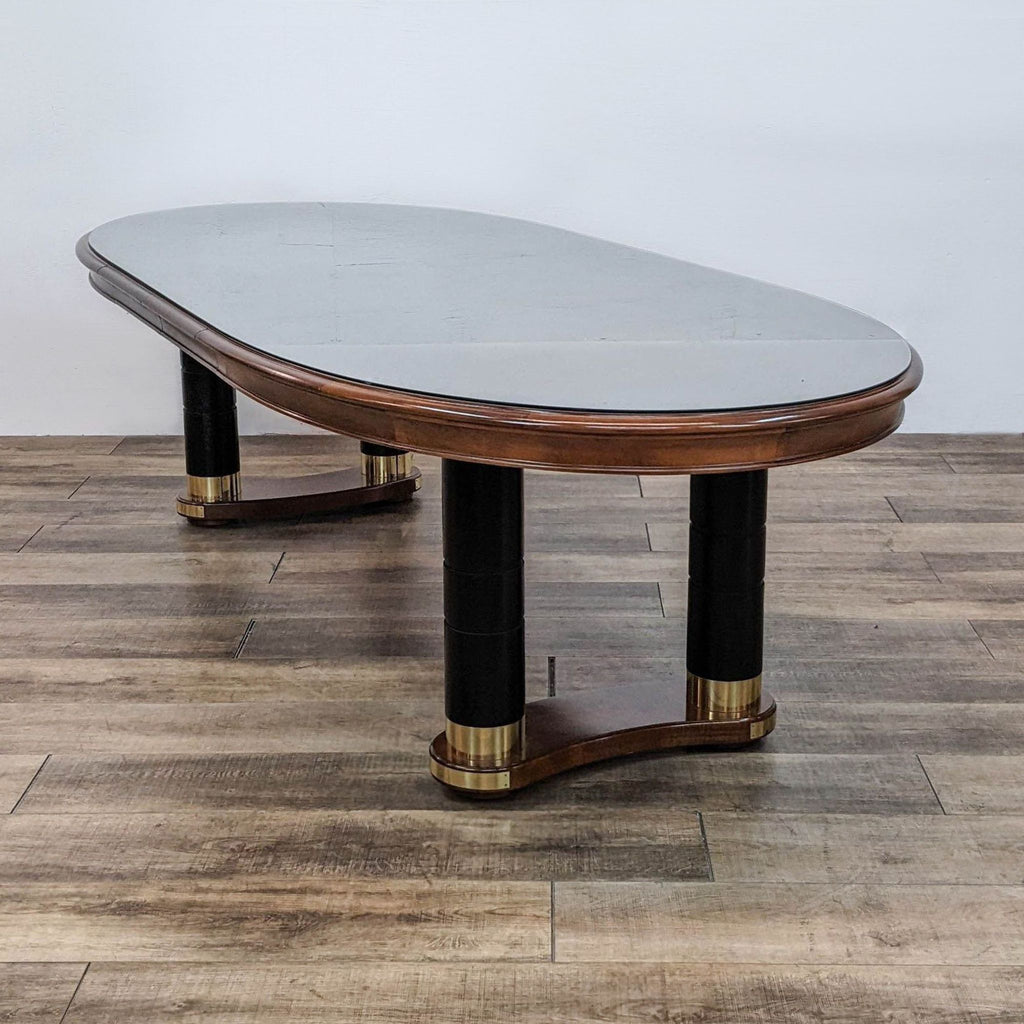 Oval cherry dining table by Stanley Furniture with black double pedestal base and brass trim, without leaf extensions.