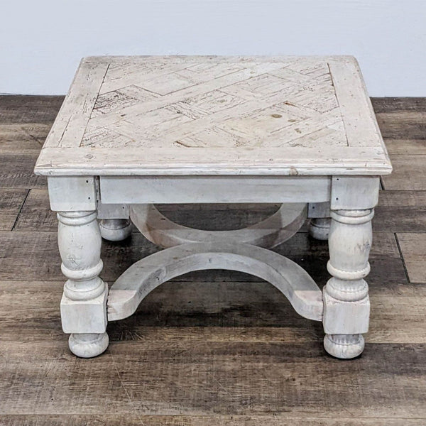 Reperch brand distressed white square side table with carved top and bulbous legs on wooden floor.