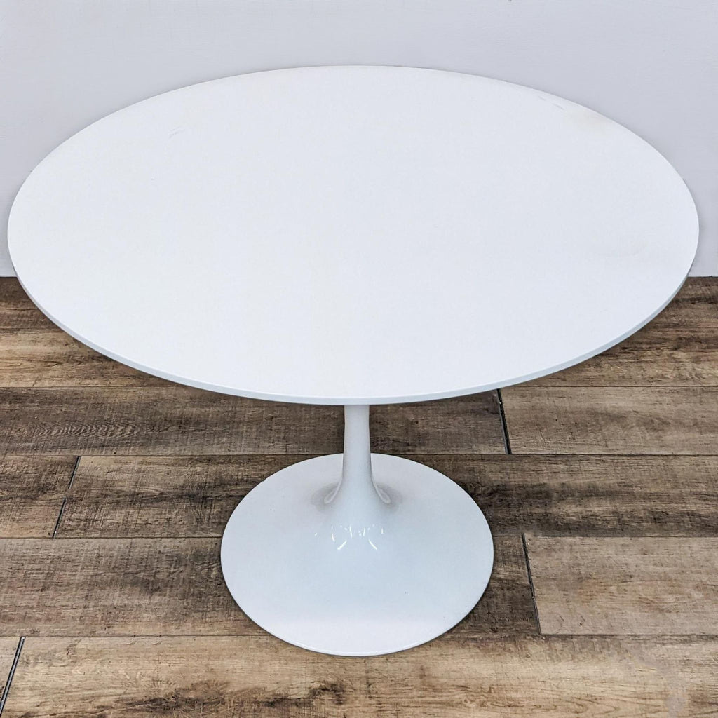 White round Reperch dining table with a stylish tulip base, against a white wall on herringbone flooring.