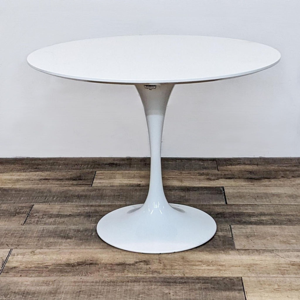 Reperch modern round white dining table with tulip base, on a wooden floor.