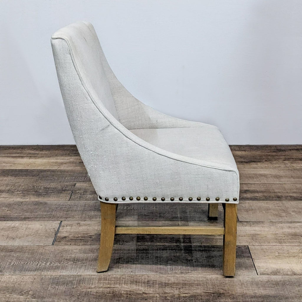 Restoration Hardware chair, side angle, showing beige fabric and wood legs on a wooden floor.