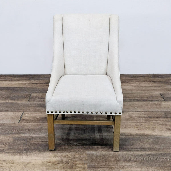 Beige upholstered chair with nailhead trim by Restoration Hardware, front view on wood floor.