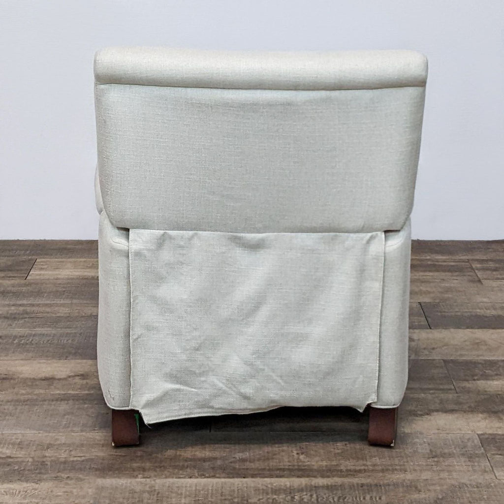 Pottery Barn light gray upholstered chair with skirted bottom and wooden legs, viewed from the back on a wooden floor.