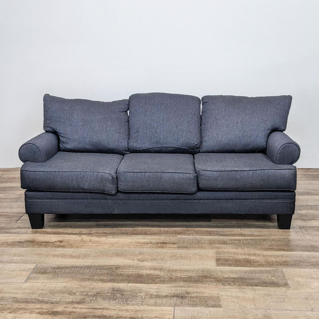 Contemporary 3-seat Living Spaces sofa with dark grey fabric and roll arms, shown in a frontal view.