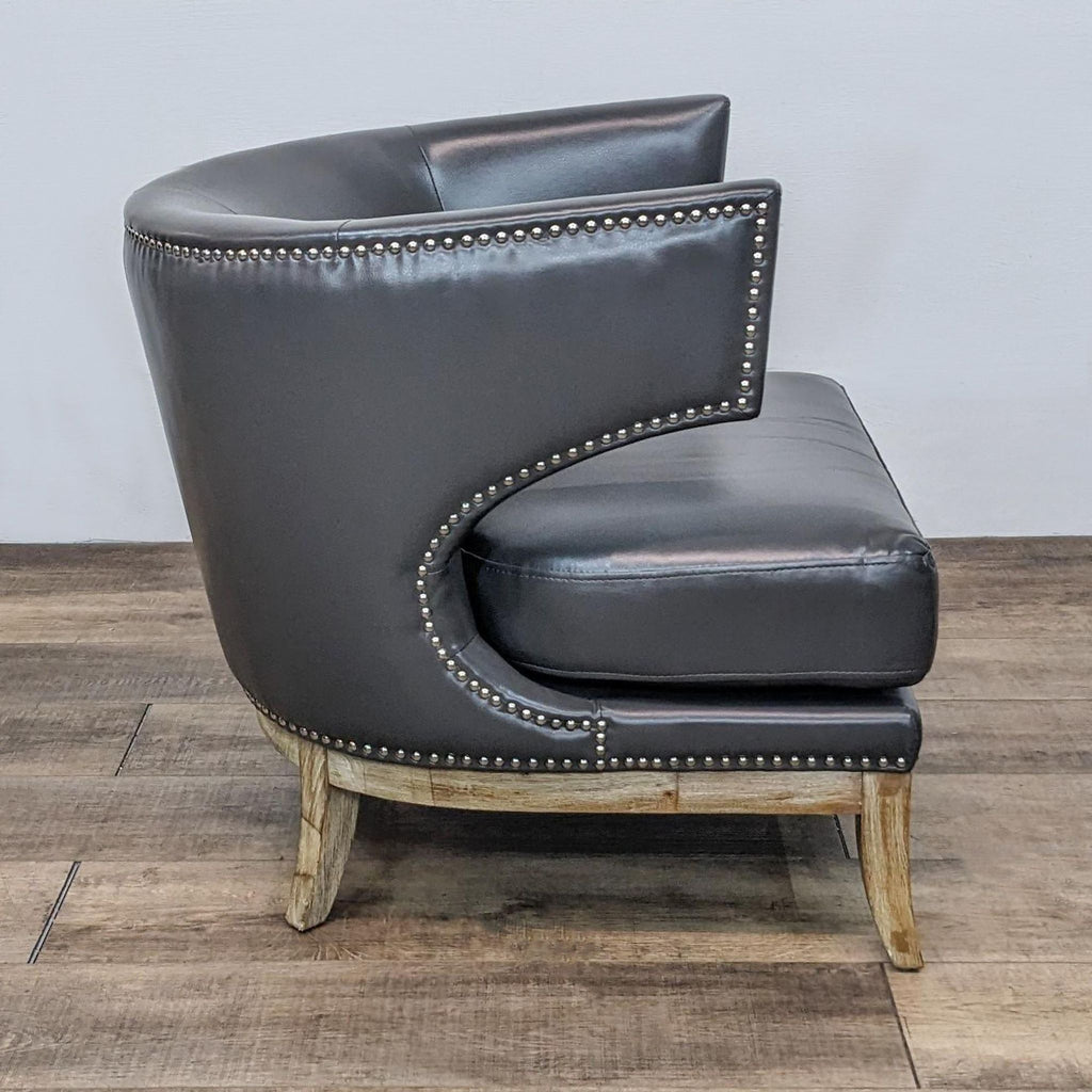 Alt text 2: Side view of a leather upholstered barrel-back Reperch lounge chair, featuring exposed nailhead trim and curvaceous weathered wooden legs.