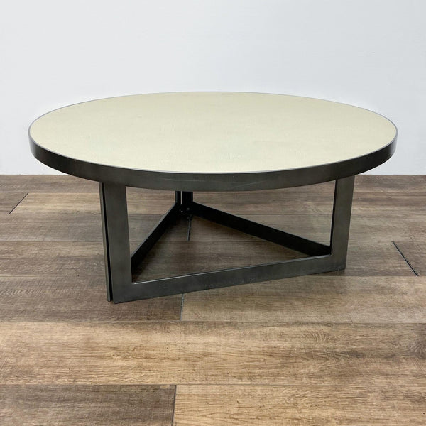 Burke Decor coffee table with ivory faux shagreen top and triangular antiqued brass-finish iron base on wooden floor.