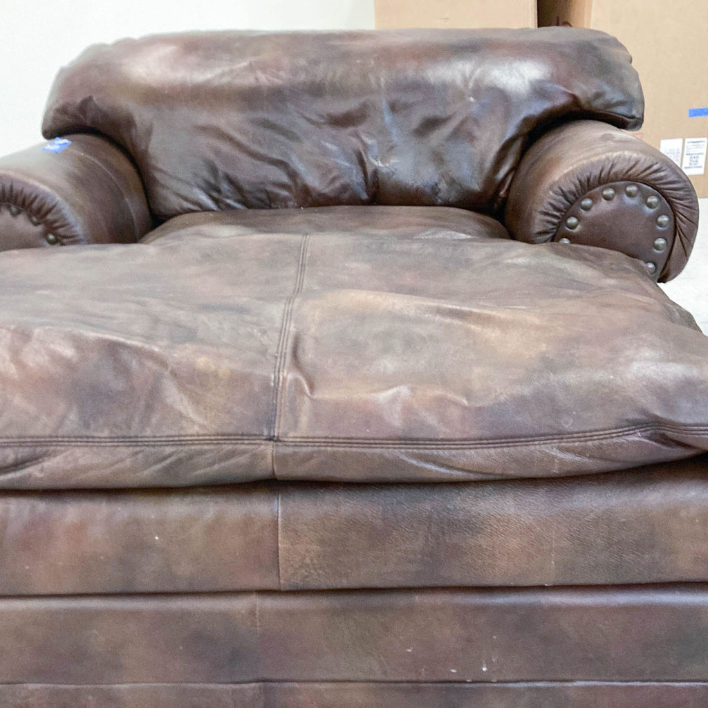 Plush Reperch chaise lounge in oversized design, upholstered in brown leather with elegant nailhead trim on rolled arms.