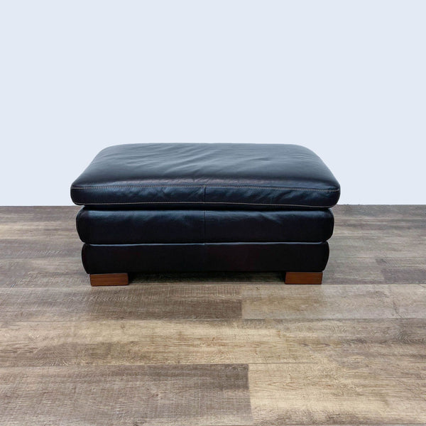 Rectangular brown leather Reperch ottoman with contrast stitching on wooden feet on a wooden floor.