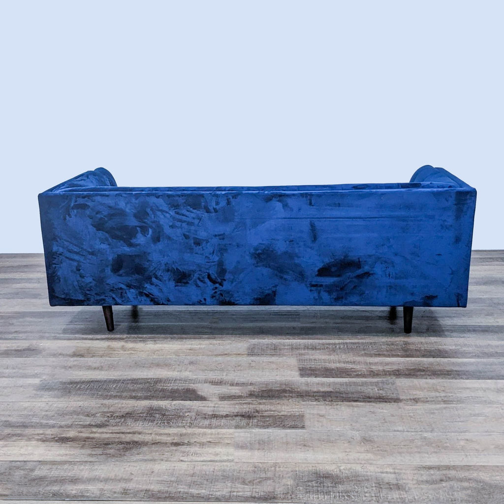 Alt text 2: Rear view of a Wayfair blue velvet 3-seater couch with tufting and modern dark legs, on a textured wood floor.