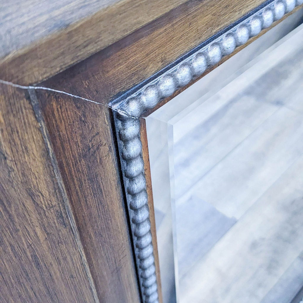 Close-up of Bombay Company's Balthasar mirror detailing antique silver beaded frame on a wooden texture.