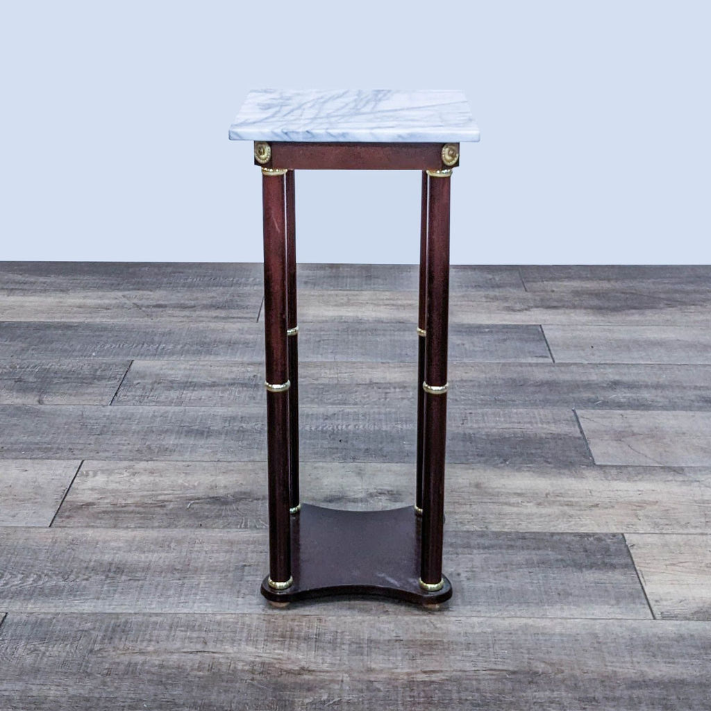 Reperch end table with marble top and wooden legs featuring brass embellishments on a wooden floor.