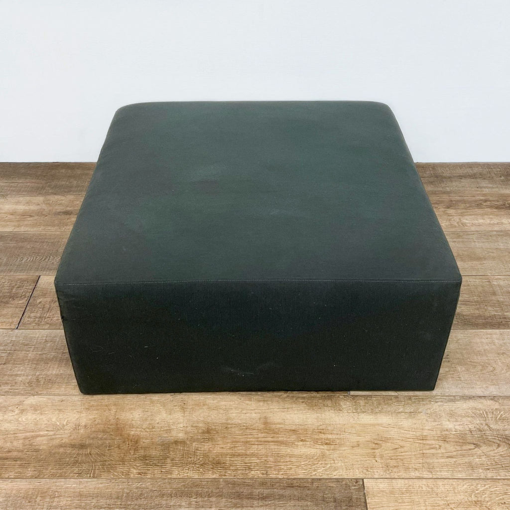 Gray square ottoman by Crate & Barrel, suitable as a coffee table, on a wooden floor.