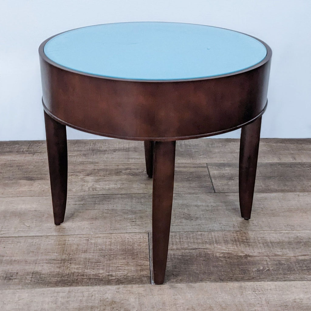 Elegant circular glass-topped end table by Reperch with tapered legs, against a neutral backdrop.