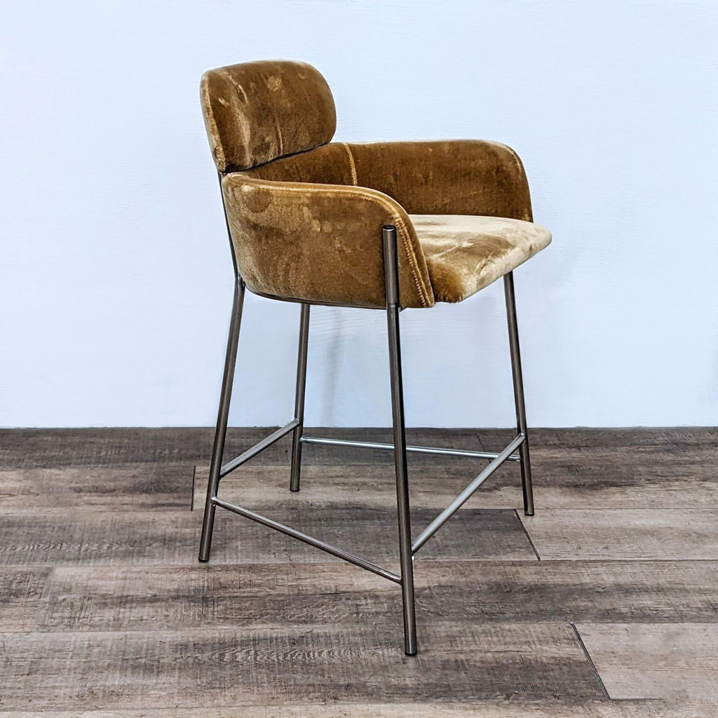CB2-designed stool with plush velvet seat and gold-tone metal legs, angled view.