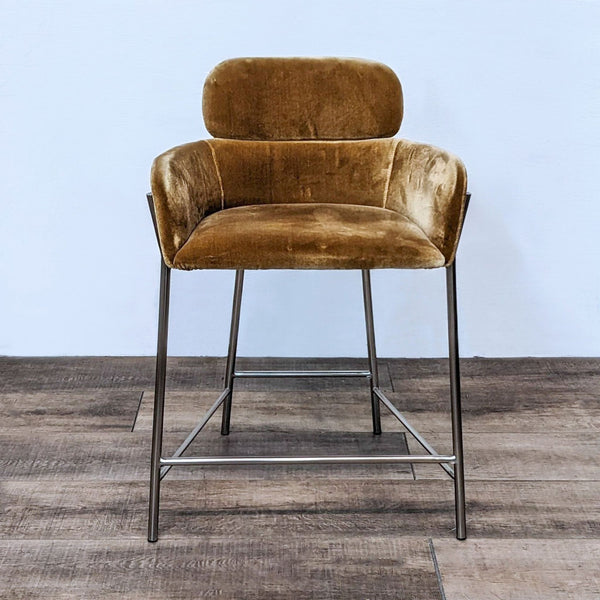 Velvet stool with gold-tone metal base by CB2, front view on wooden floor.