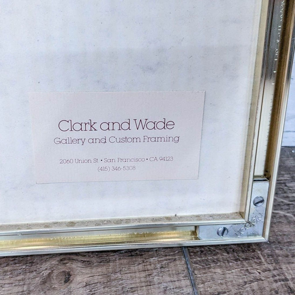 Close-up of a gallery label from Clark and Wade inside a picture frame, on a textured papyrus paper background.