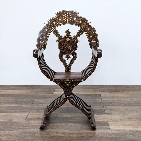Front view of a Reperch Savonarola chair with brass inlay, showcasing intricate detailing, on a wooden floor.
