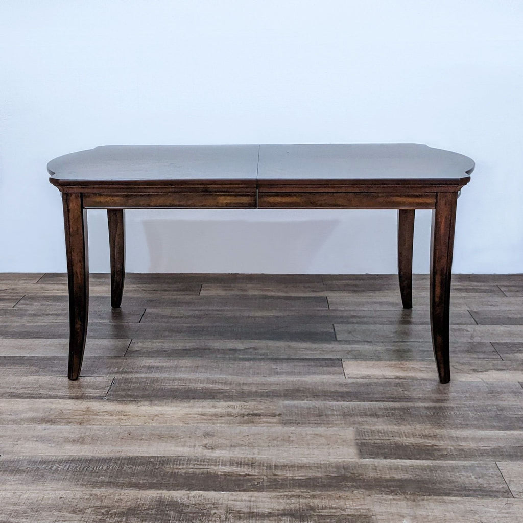 Reperch brand dining table with curved ends and tapered legs, shown closed on wooden floor.