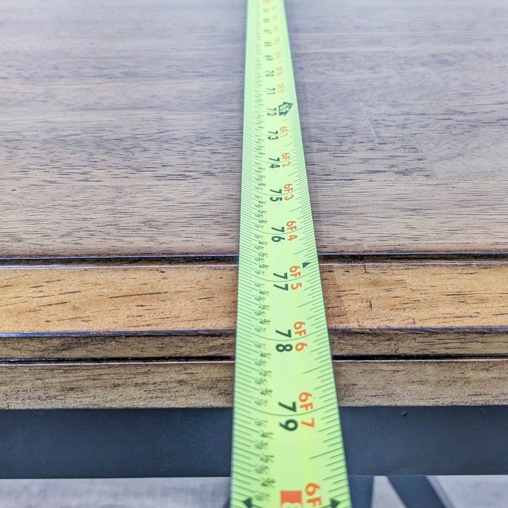 Alt text 2: Close-up of the table edge from Winners Only dining set, showcasing the wood finish and black base with a measuring tape.