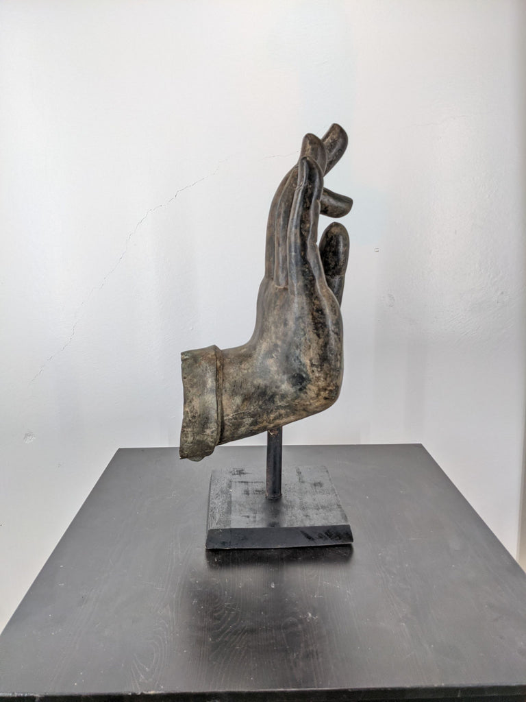 2. Side view of a large bronze Buddha hand sculpture on a granite base, showing vitarka mudra gesture.