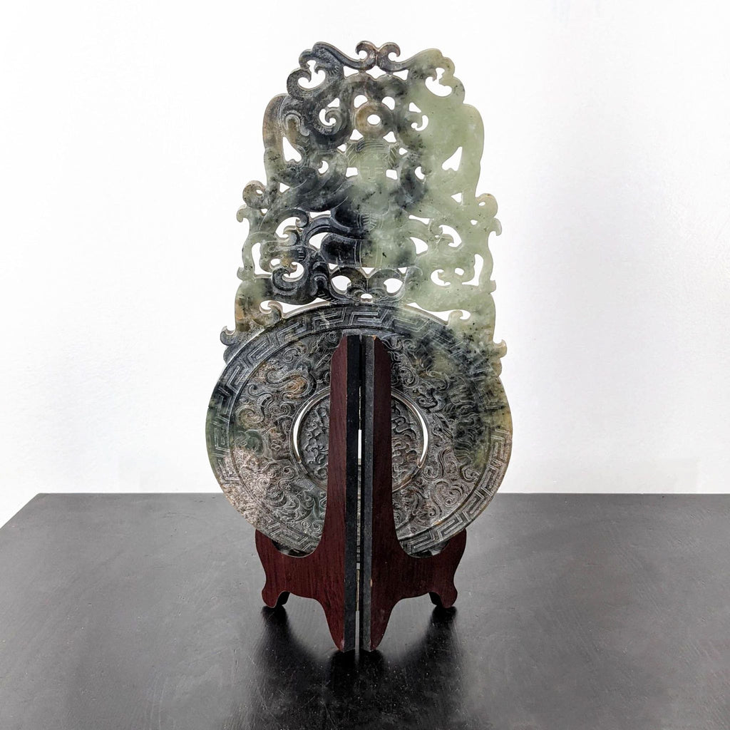 3. Ornately carved jade disc by Reperch, featuring intricate patterns and shapes, displayed on a wooden stand.
