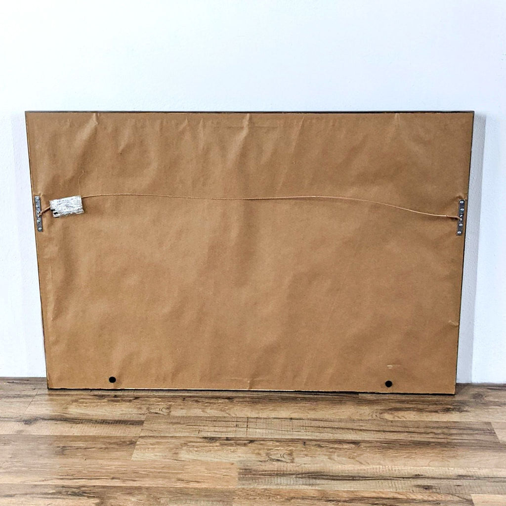 Back of the framed cowboy and horses painting, showing brown paper backing and a hanging wire attached.