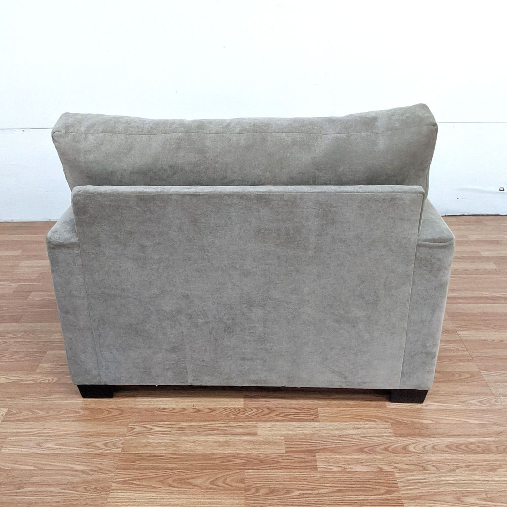 Rear view of a grey Reperch brand lounge armchair against a white wall and wooden floor.