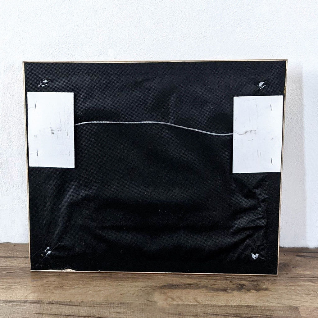 The back view of a Reperch drawing or painting with a black canvas and a hanging wire.