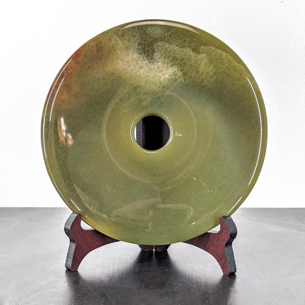 1. Circular green jade disc by Reperch, polished with a central hole, displayed upright on a dark wooden stand.